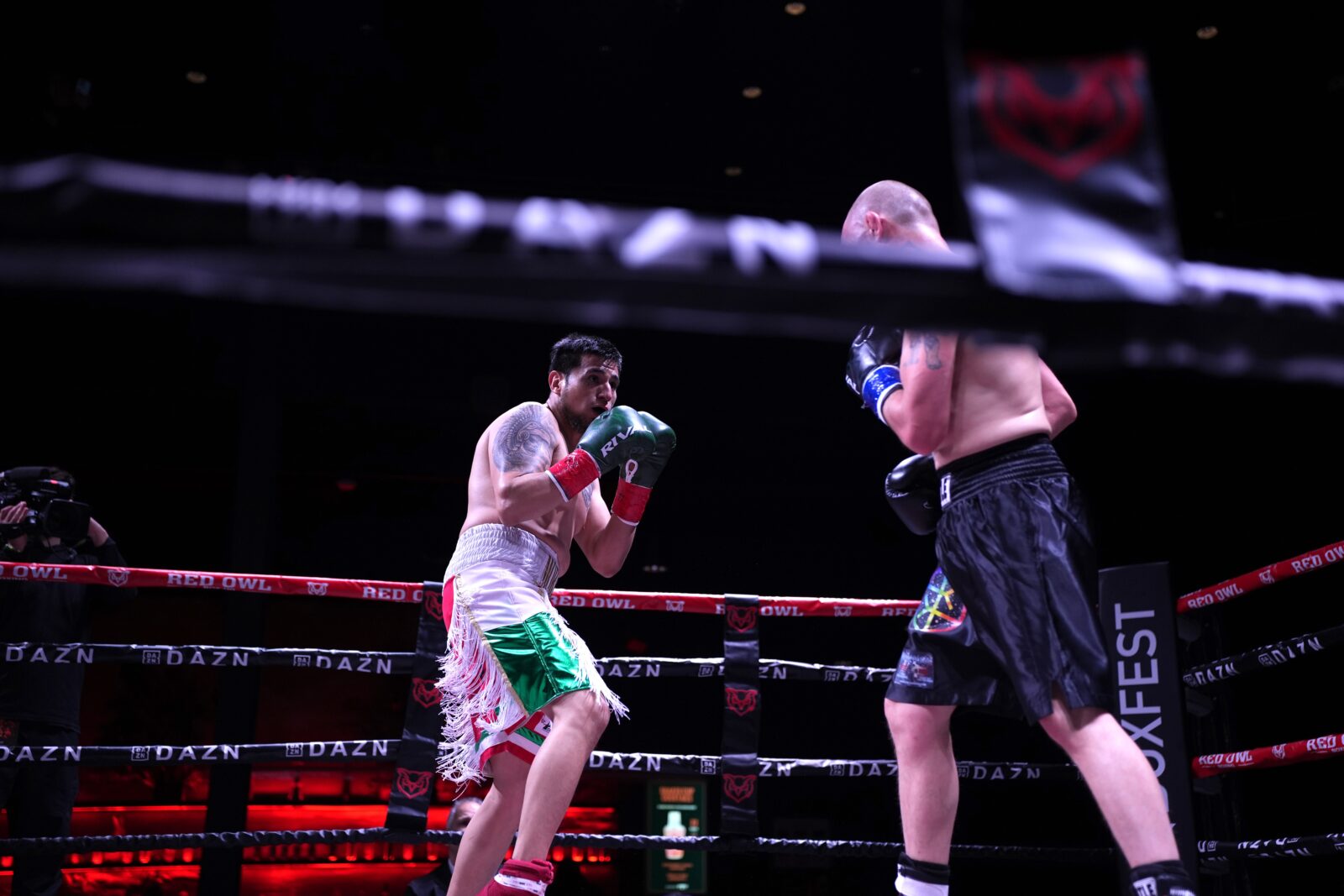 gustavo morales in white and green shorts stalks forward with gloves raised toward chevy bridges in black shorts under the dazn and boxfest signage at archer music hall