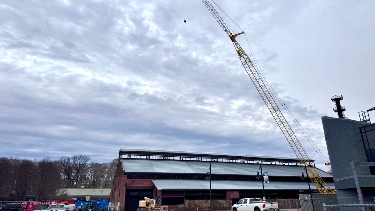 a construction crane rises above the brick turn & grind shop building at steelstacks in bethlehem, with a partially installed metal roof, work vehicles and fencing in the foreground under an overcast sky