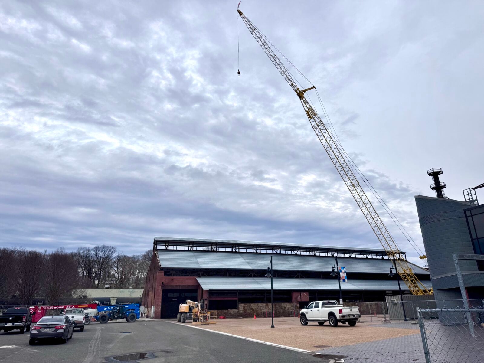a construction crane rises above the brick turn & grind shop building at steelstacks in bethlehem, with a partially installed metal roof, work vehicles and fencing in the foreground under an overcast sky
