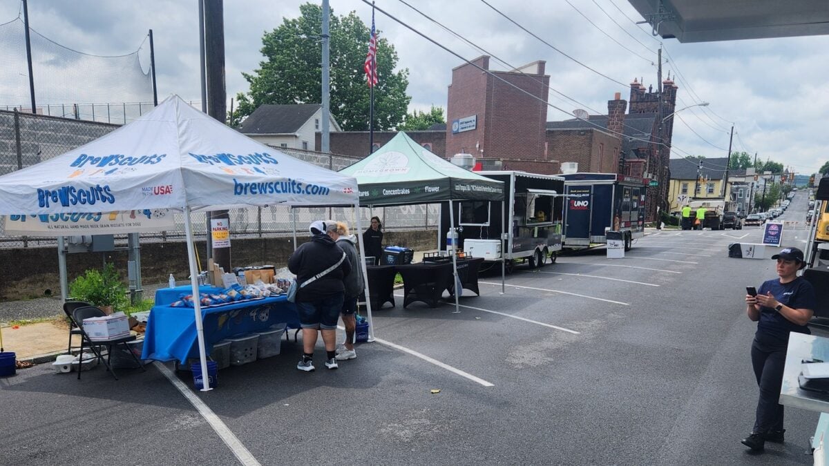 vendor tents and food trailers set up along a closed street, with two people browsing a tent table and a worker standing nearby