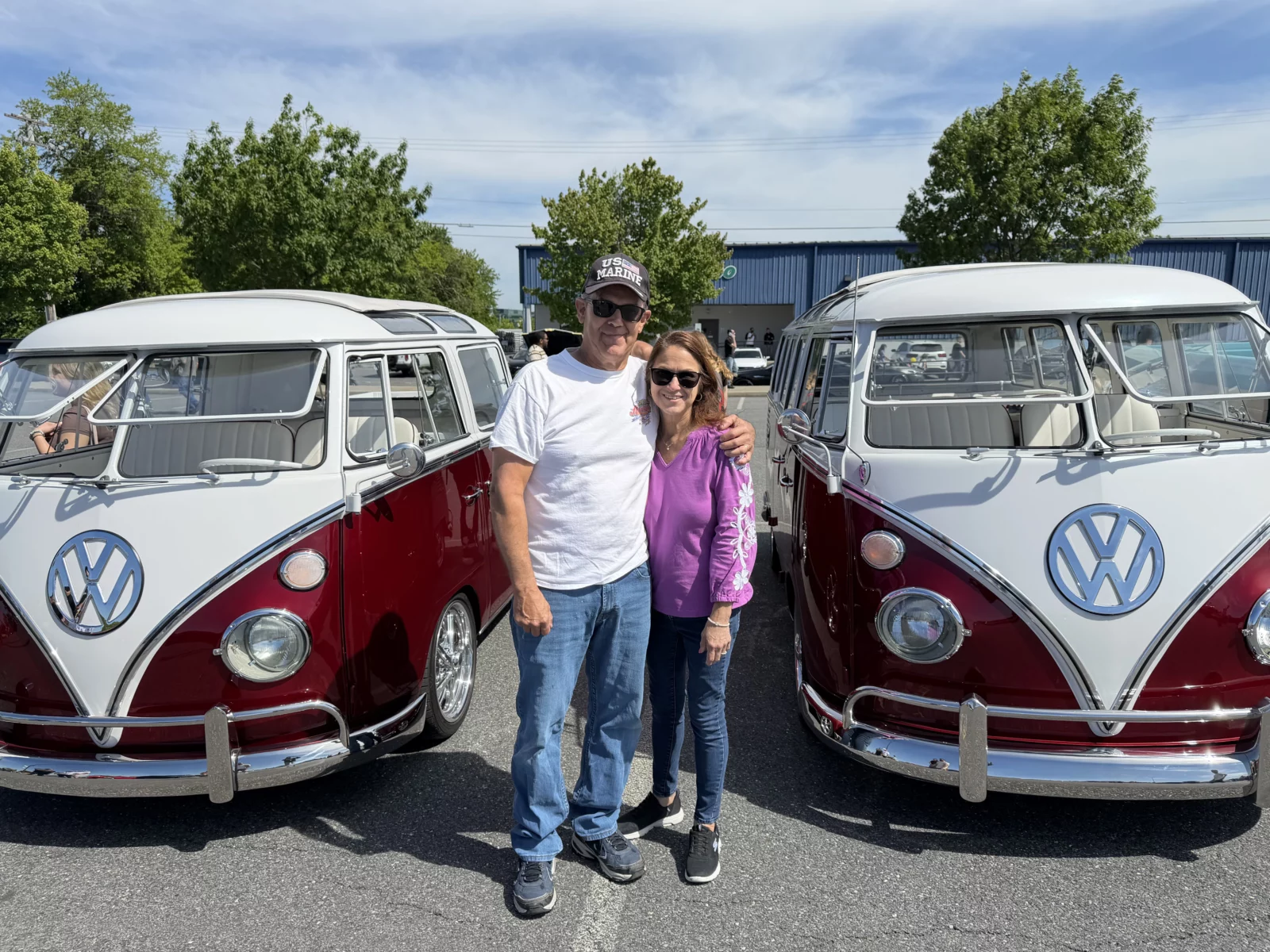Brian and Annette Brensinger stand arm in arm between their two restored red-and-white Volkswagens at a car show