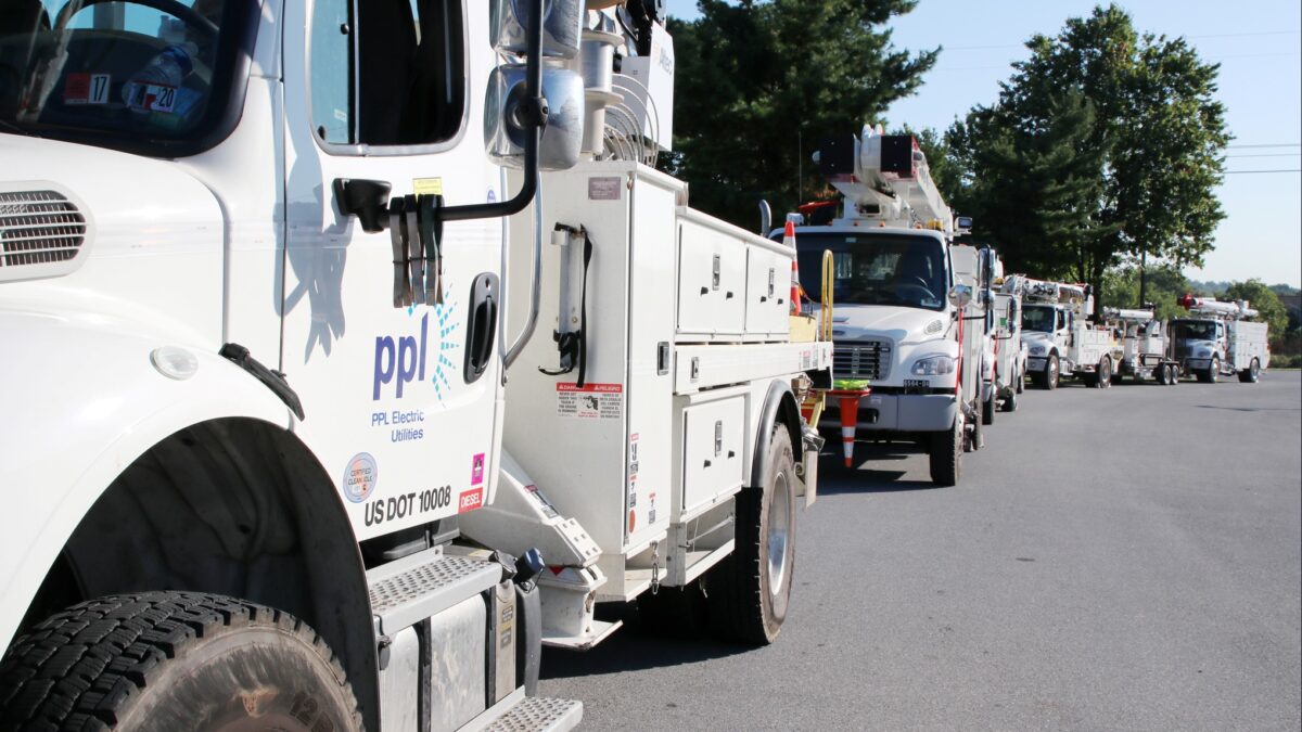 a row of white ppl electric utilities line trucks parked end to end along a road on a sunny day