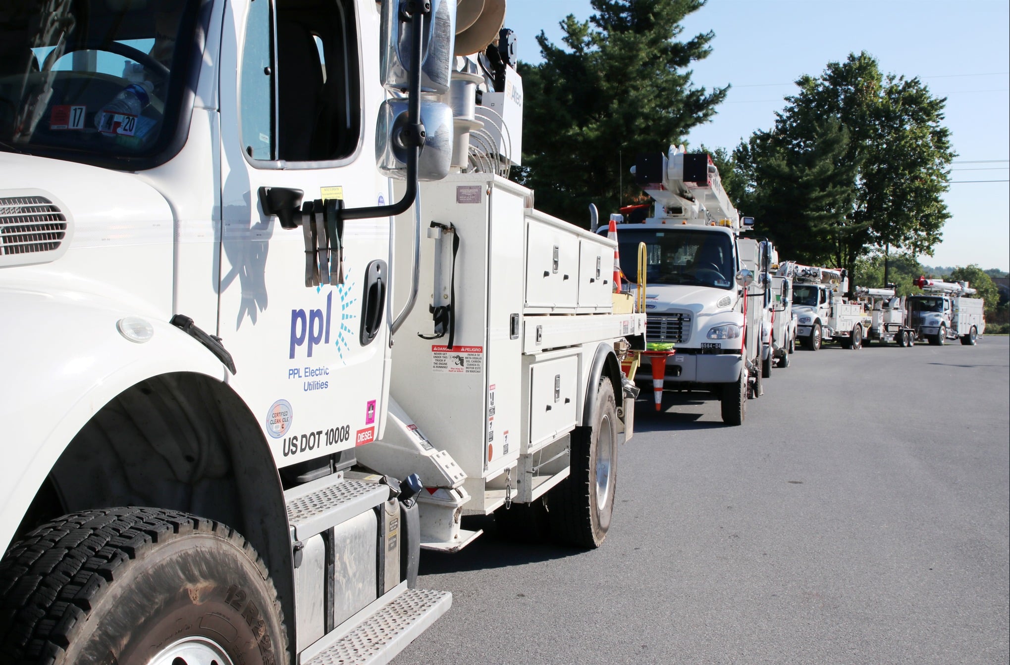 a row of white ppl electric utilities line trucks parked end to end along a road on a sunny day