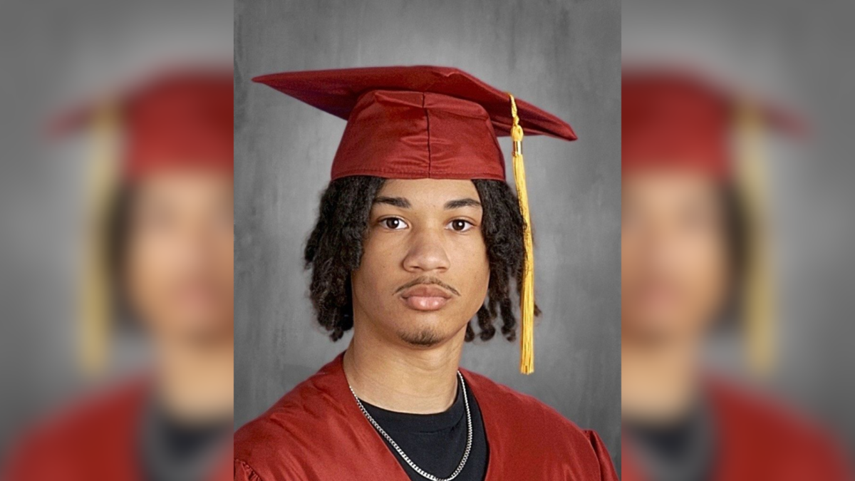 Tymell Millan-Mason poses for his Lincoln Leadership Academy Class of 2026 senior portrait, wearing a red graduation cap and gown with a gold tassel over a black t-shirt and silver chain.