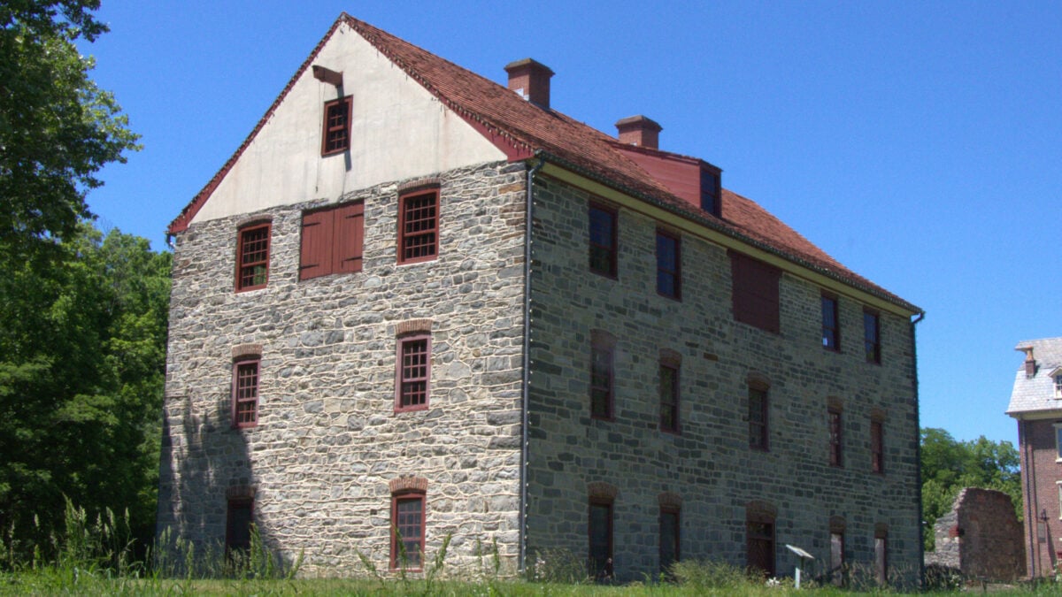 Old stone building with a red tile roof and red shutters under a clear blue sky.