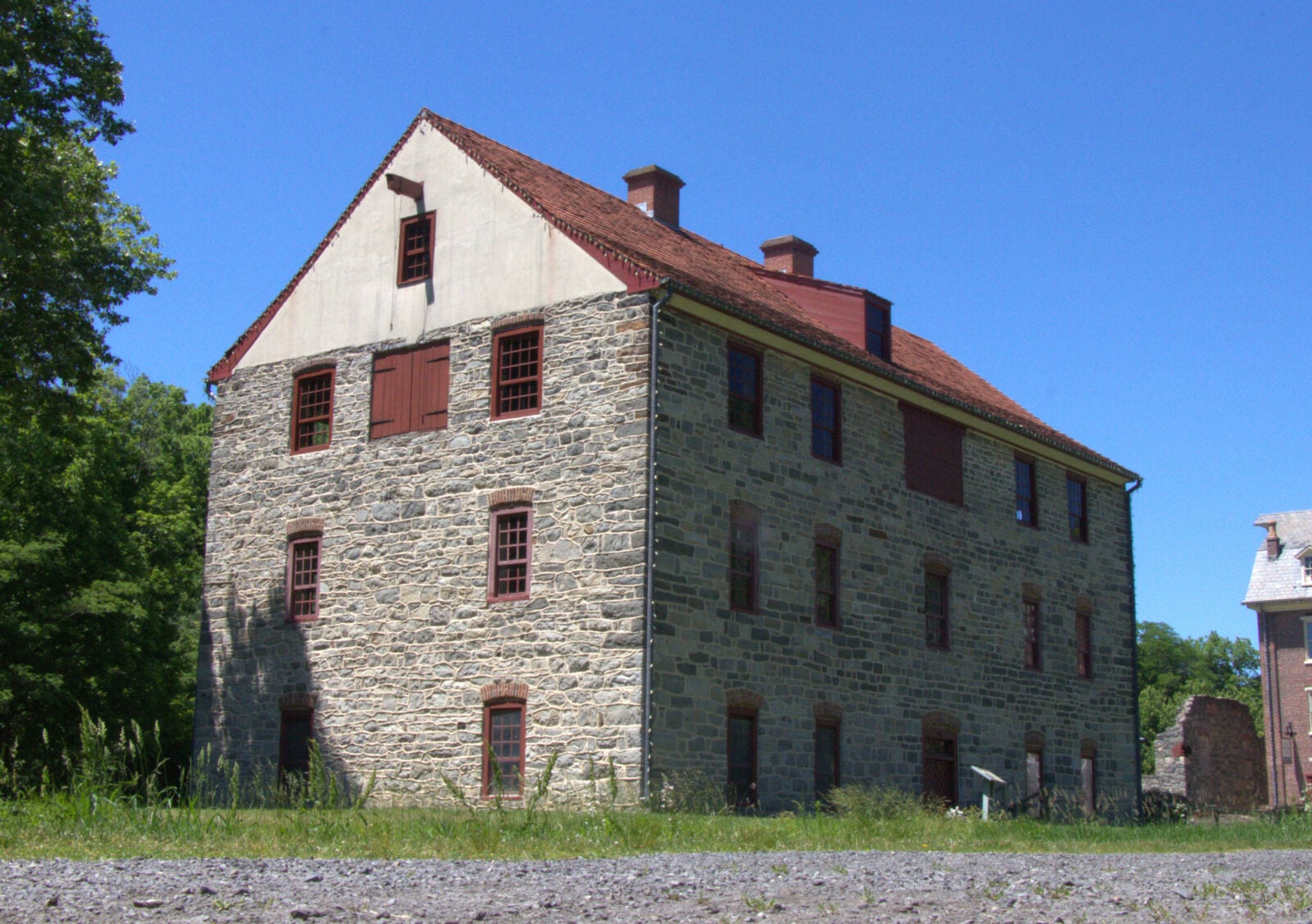 Old stone building with a red tile roof and red shutters under a clear blue sky.