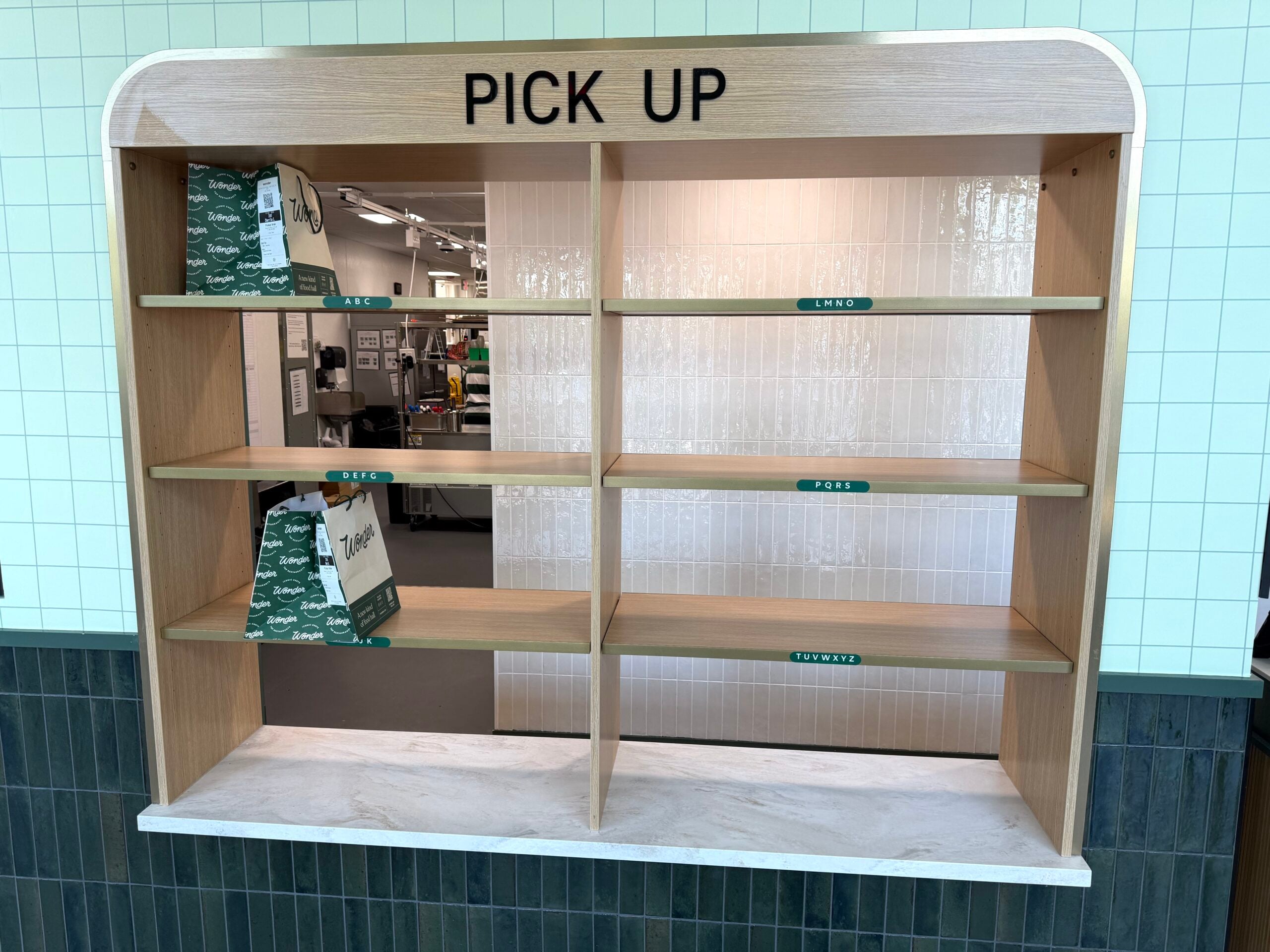 A wooden shelving unit labeled 'PICK UP' holds two green and white Wonder bags.