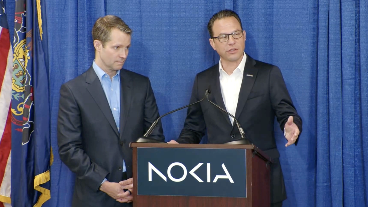 Two men in suits stand at a podium with the Nokia logo, one speaking.