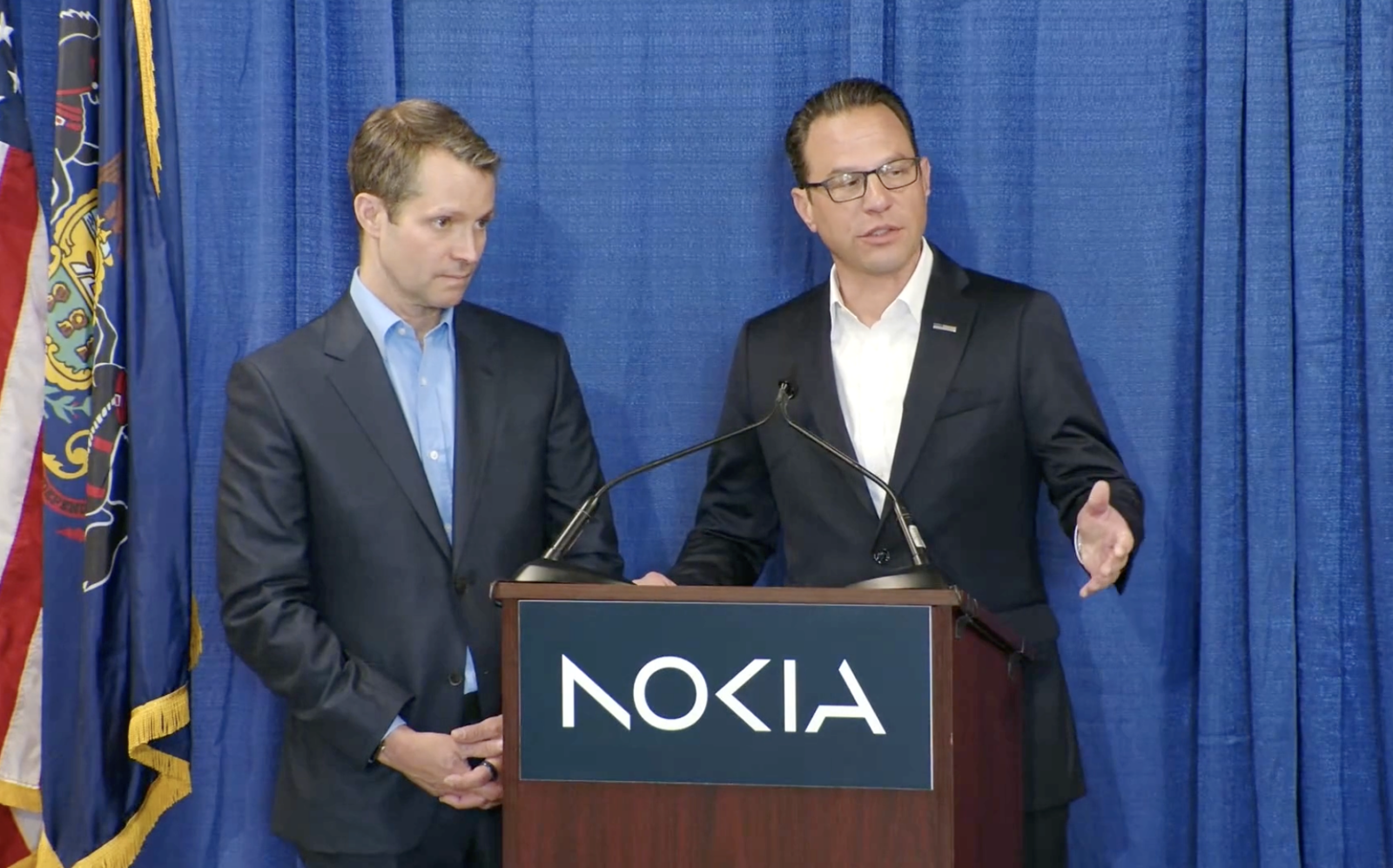 Two men in suits stand at a podium with the Nokia logo, one speaking.