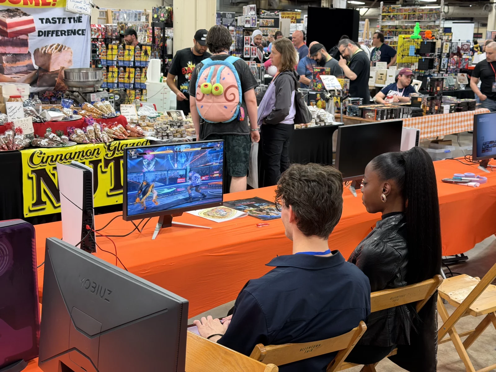 Two people play Tekken on a monitor at a convention gaming station.