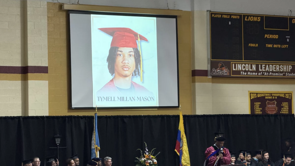 A large screen displays a portrait of Tymell Millan-Mason at a graduation ceremony.