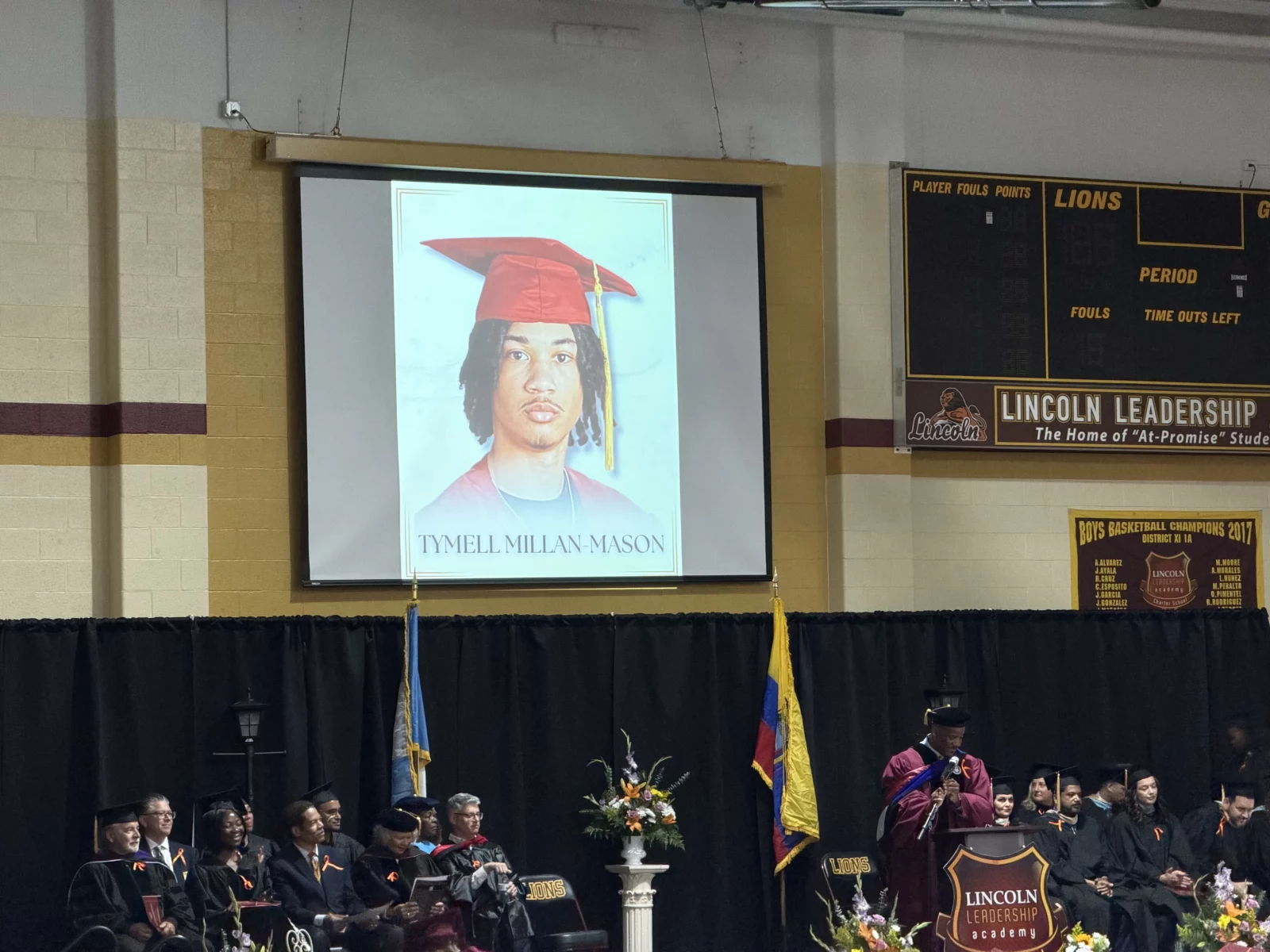 A large screen displays a portrait of Tymell Millan-Mason at a graduation ceremony.