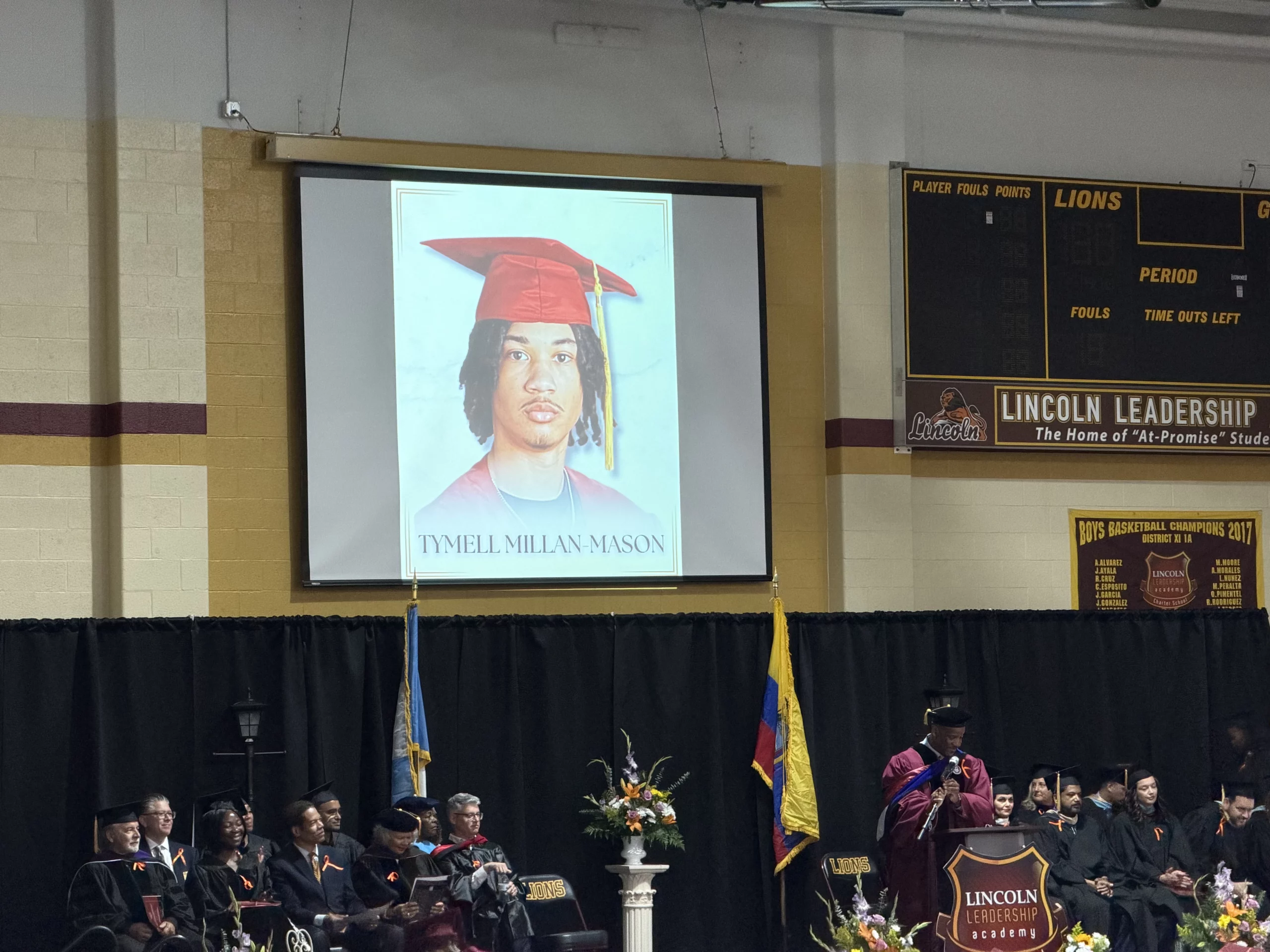 A large screen displays a portrait of Tymell Millan-Mason at a graduation ceremony.