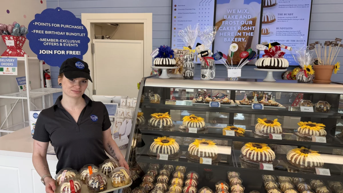 Bakery Manager Libby Schwartz holds a tray of Bundtlets in front of a bakery display case at Nothing Bundt Cakes in Easton.