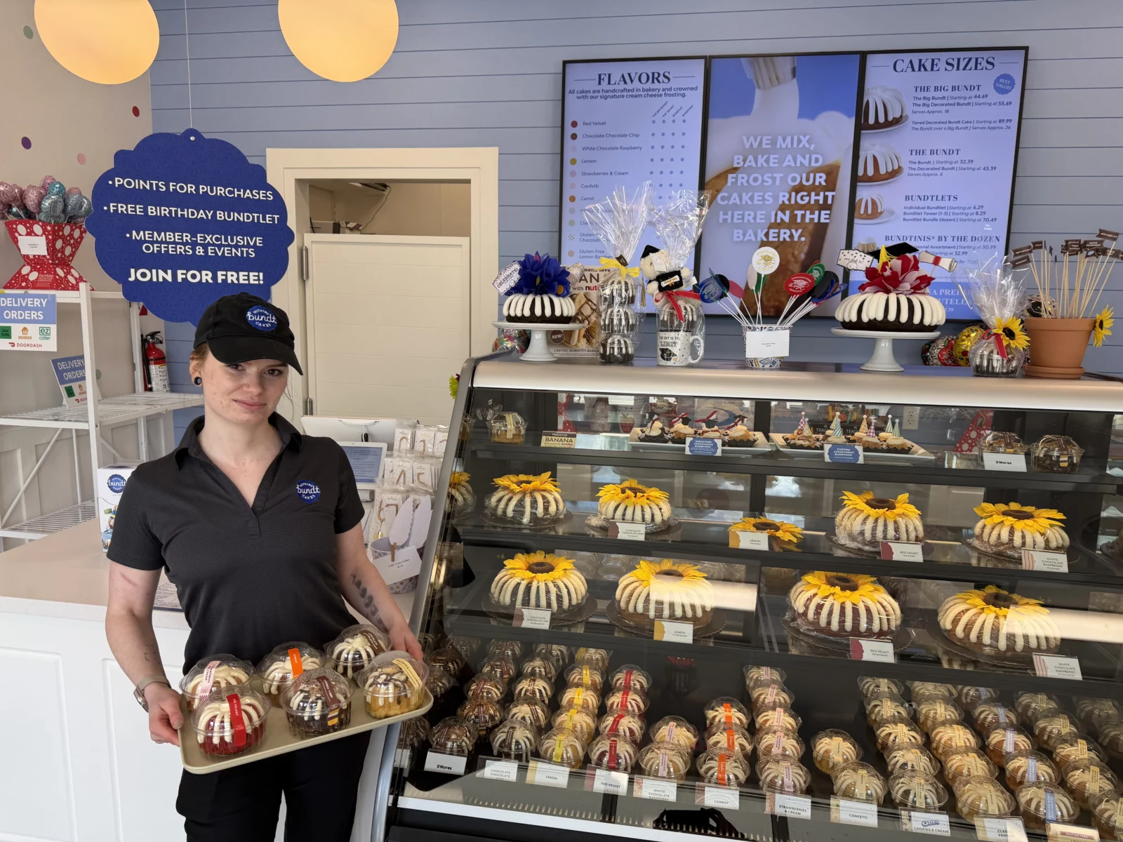Bakery Manager Libby Schwartz holds a tray of Bundtlets in front of a bakery display case at Nothing Bundt Cakes in Easton.