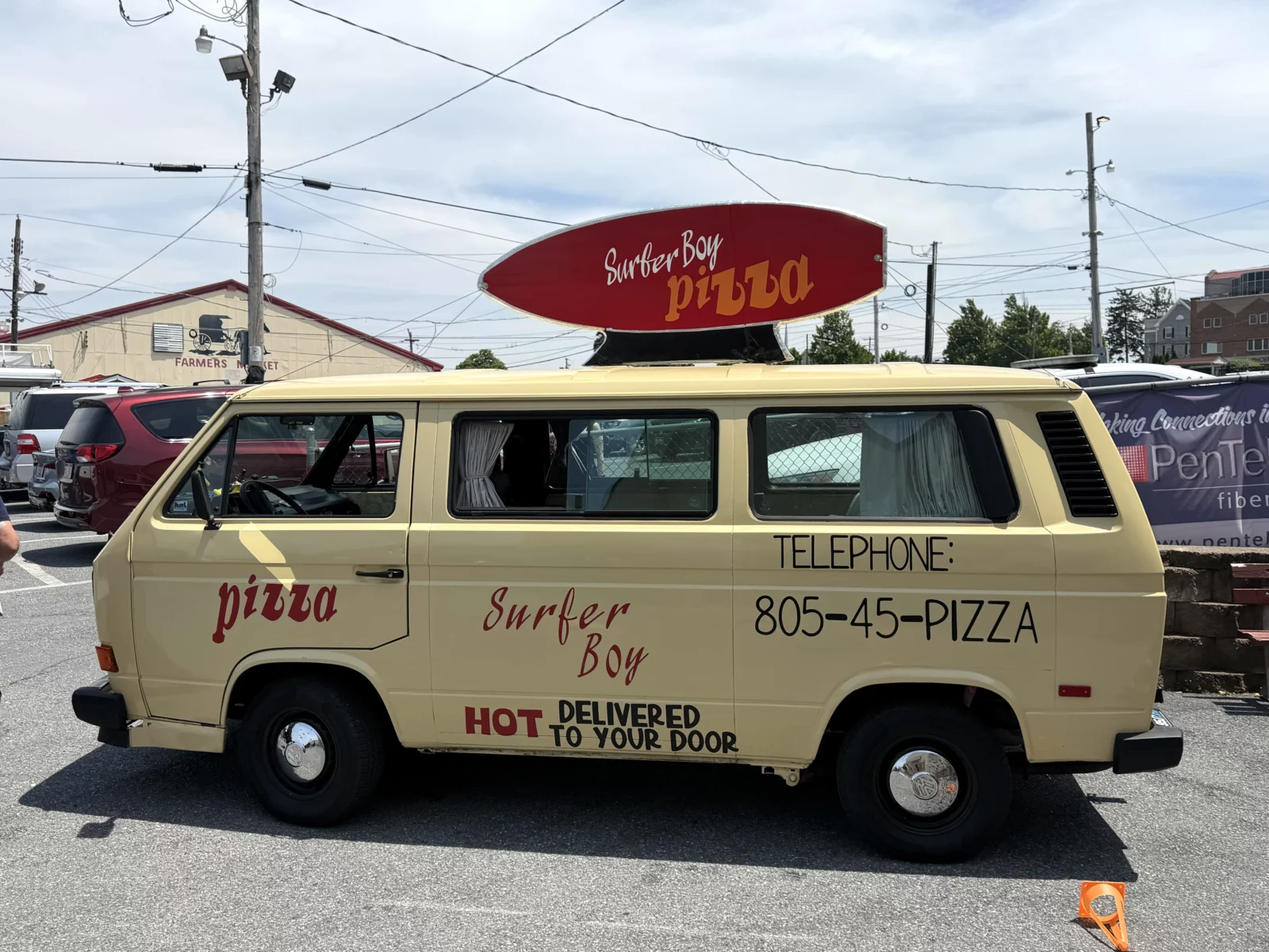 Light yellow Volkswagen van with "Surfer Boy Pizza" branding and a surfboard sign on the roof.
