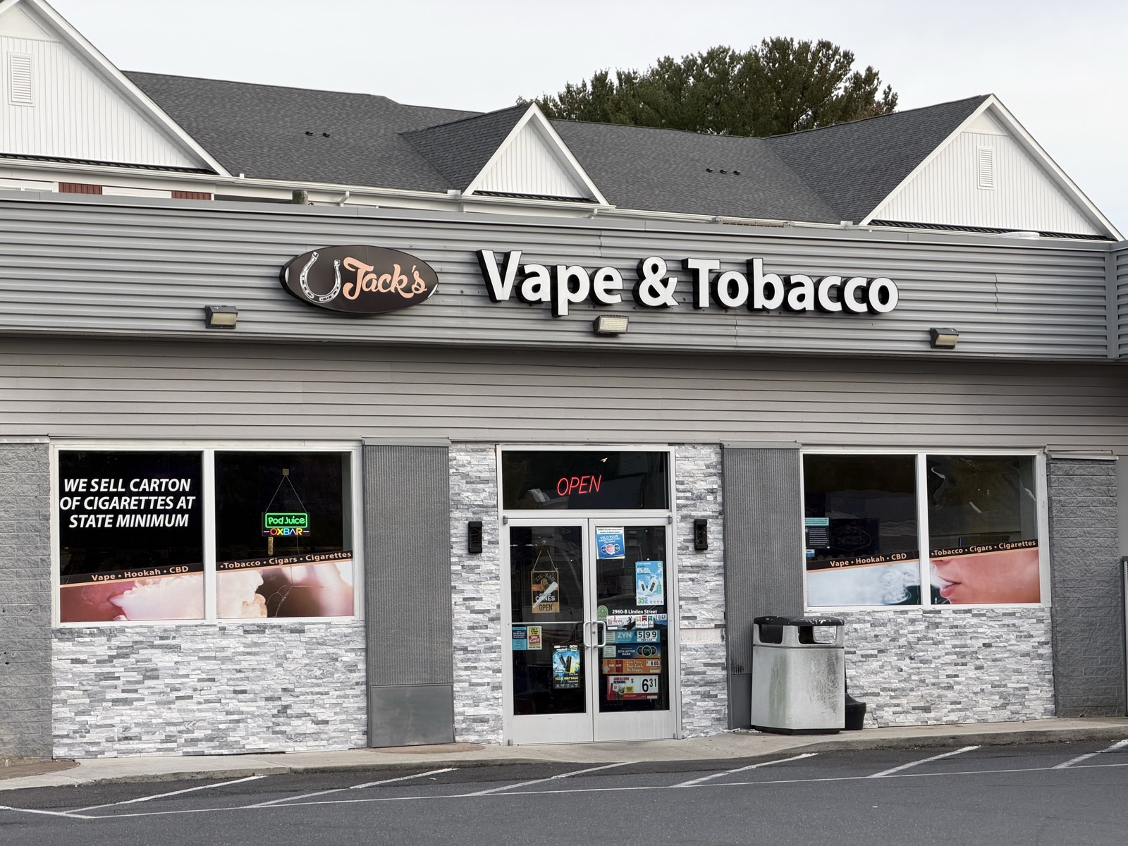 Exterior of a gray one-story shop with a Vape & Tobacco sign and an open sign in the door.