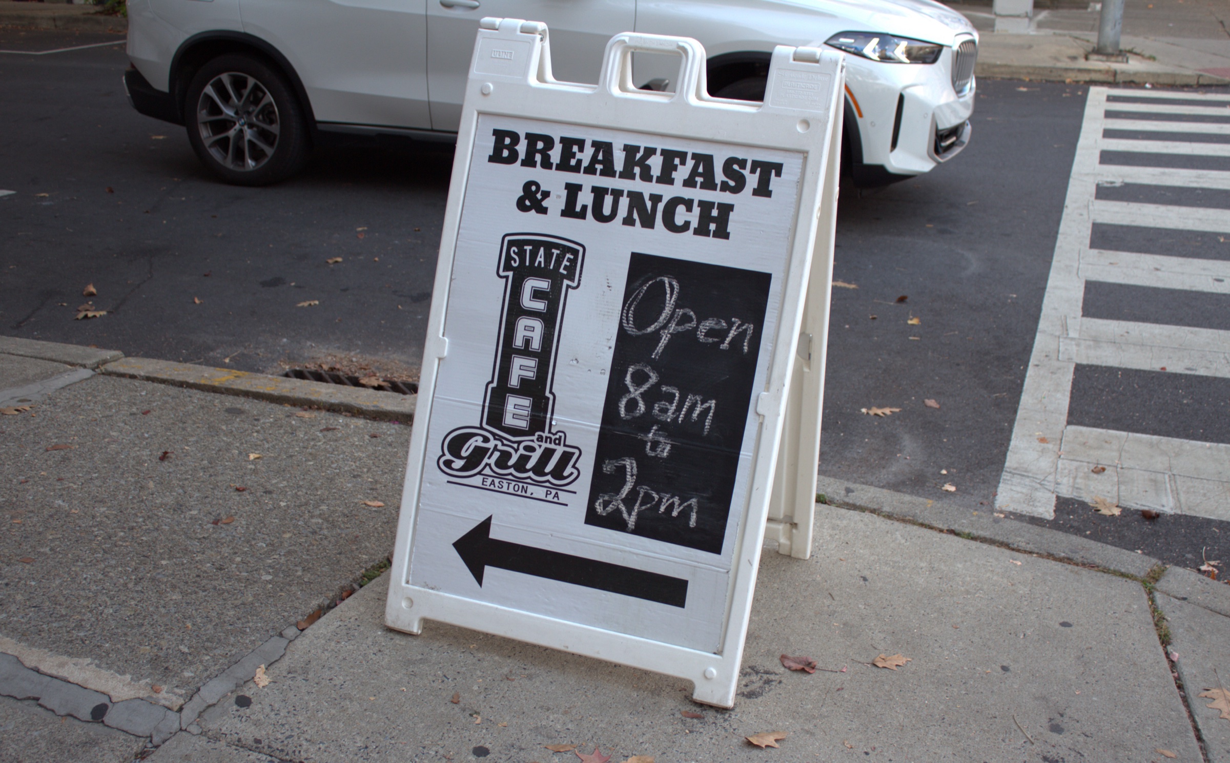 A sidewalk sign reading "Breakfast & Lunch" with the State Cafe and Grill logo and "Open 8am to 2pm" chalked on it, beside a crosswalk.