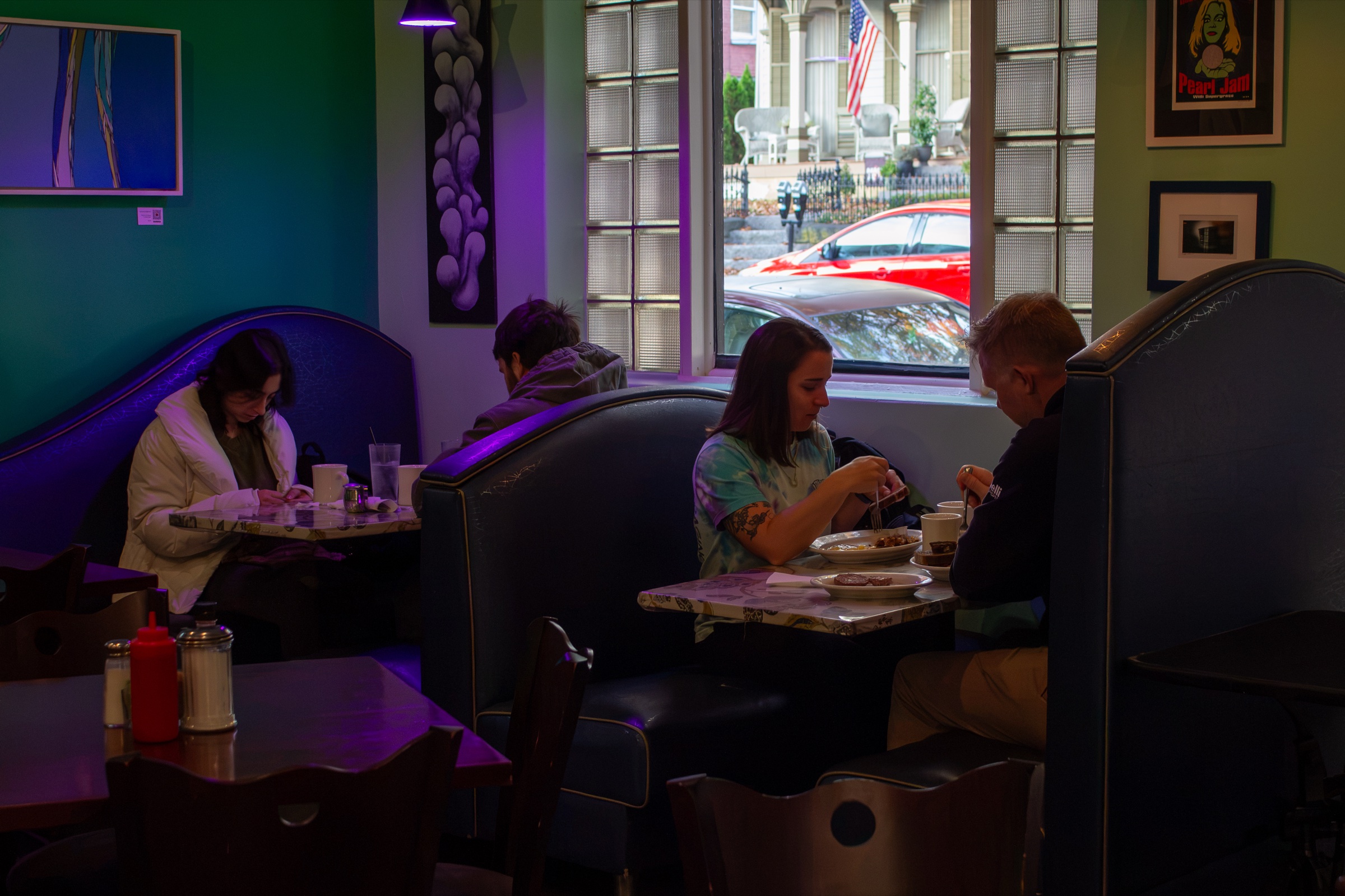 Customers eat at booths by a window in a dimly lit dining room with purple lighting and art on the walls.